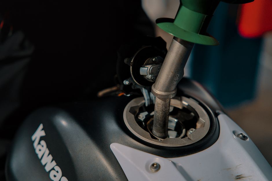 Close-up of refueling a Kawasaki motorcycle at a gas station, with nozzle inserted into the tank.